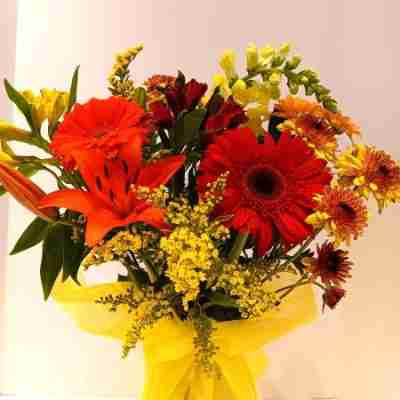 The Hint of Fall Bouquet displayed in a decorated yellow vase against a white background